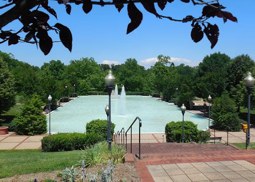 Scenic view of a large reflecting pond at Quiet Waters Park with fountains, surrounding greenery, walking paths, and overhead tree branches.